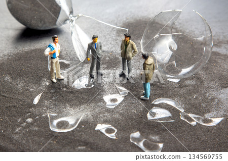 Miniature figures gather around shattered glass in a dramatic setting Miniature figures gather around shattered glass in a dramatic setting 134569755