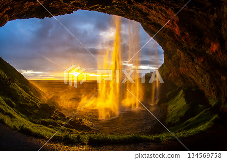 Majestic waterfall cascading from a cave with a sunset glow in Iceland Majestic waterfall cascading from a cave with a sunset glow in Iceland 134569758