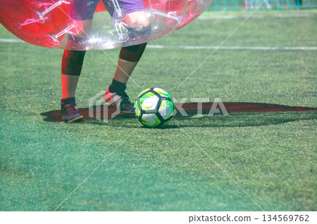 Players engaged in bubble soccer on a sunny day at a sports field 134569762