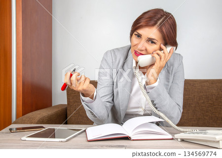 Businesswoman engaged in a phone conversation while working at a modern office desk Businesswoman engaged in a phone conversation while working at a modern office desk 134569774