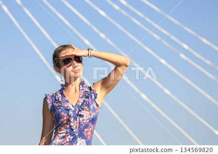 Woman shielding eyes from sun while standing under bridge on a bright day Woman shielding eyes from sun while standing under bridge on a bright day 134569820