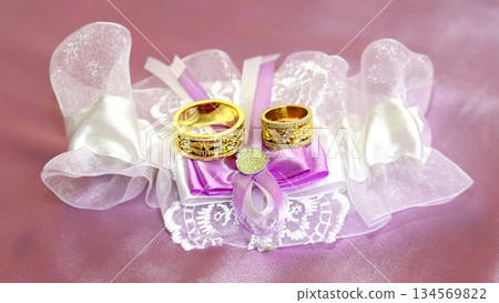 Gold wedding rings displayed on elegant satin and lace fabric with purple accents Gold wedding rings displayed on elegant satin and lace fabric with purple accents 134569822
