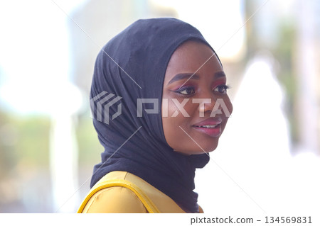 African woman wearing a hijab smiling outdoors during daytime in a vibrant urban setting 134569831