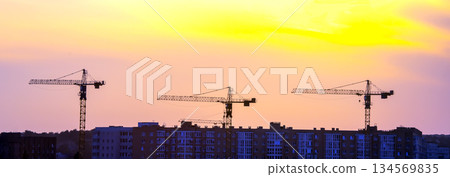 Construction cranes silhouetted against a vibrant sunset in an urban landscape Construction cranes silhouetted against a vibrant sunset in an urban landscape 134569835
