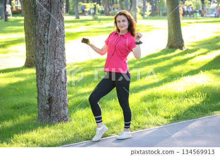 Young woman enjoying a sunny day in the park while listening to music and dancing Young woman enjoying a sunny day in the park while listening to music and dancing 134569913