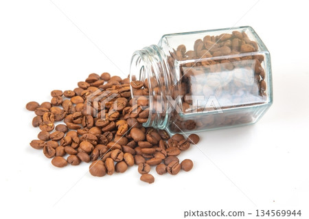 Brown coffee beans spilling from a glass jar on a white background Brown coffee beans spilling from a glass jar on a white background 134569944
