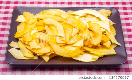Freshly prepared slices of pumpkin arranged on a purple plate on a checkered tablecloth 134570017