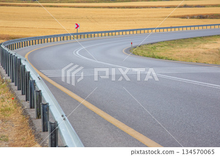 Curve in the road surrounded by golden fields on a clear day Curve in the road surrounded by golden fields on a clear day 134570065