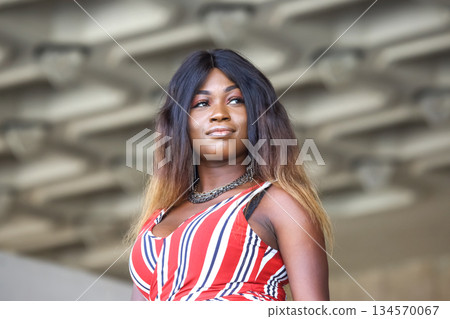 African woman posing confidently in a stylish outfit at an urban location during daylight 134570067