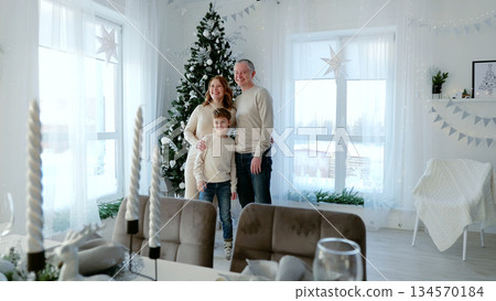 Family happily poses in a festive dining room, surrounded by a christmas tree's glow. The cozy scene is filled with love, creating special holiday memories. A day with family before Christmas. Family happily poses in a festive dining room, surrounded by a christmas tree's glow. The cozy scene is filled with love, creating special holiday memories. A day with family before Christmas. 134570184