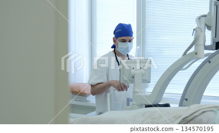 Russia Tomsk 05.07.2025: Biomedical technician calibrating surgical display equipment, scrubbed staff wearing mask and cap, hands on control panel, diagnostic status indicators and cables Russia Tomsk 05.07.2025: Biomedical technician calibrating surgical display equipment, scrubbed staff wearing mask and cap, hands on control panel, diagnostic status indicators and cables 134570195