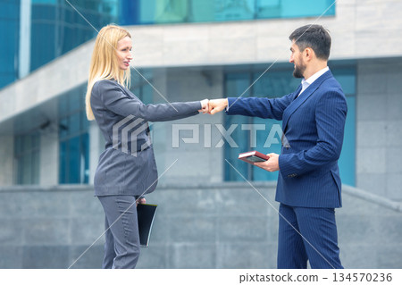 Business professionals exchanging a fist bump outside a modern building during the day Business professionals exchanging a fist bump outside a modern building during the day 134570236