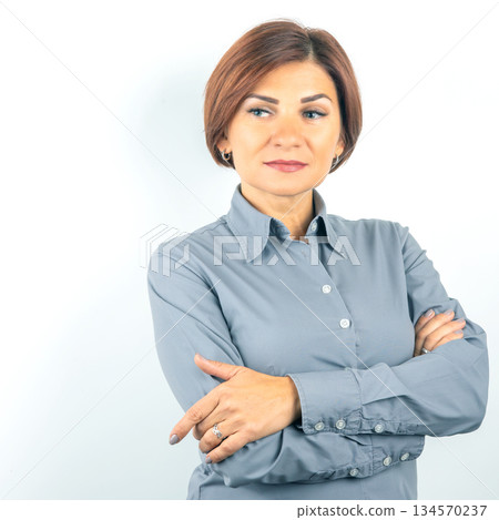 Confident businesswoman with arms crossed in formal attire standing against plain backdrop Confident businesswoman with arms crossed in formal attire standing against plain backdrop 134570237