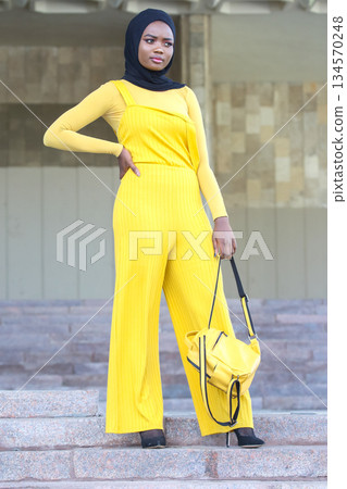 Stylish African woman in bright yellow outfit poses confidently on steps outdoors 134570248