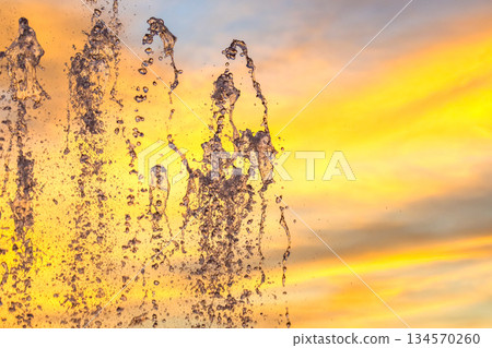 Water fountain sprays against colorful sunset sky with clouds and hues of orange and pink Water fountain sprays against colorful sunset sky with clouds and hues of orange and pink 134570260