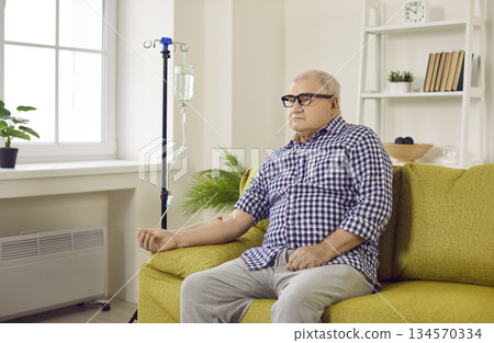 Senior man sitting on couch with iv drip attached on his hand 134570334