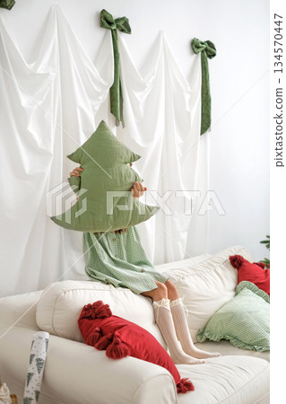 A girl shows a green pillow in the shape of a Christmas tree, greeting and calling for the new year. A girl shows a green pillow in the shape of a Christmas tree, greeting and calling for the new year. 134570447