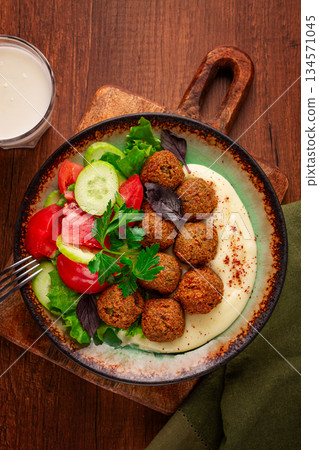 Healthy meal with falafel, tahini, salad, and drink on wooden table in cozy setting at lunchtime Healthy meal with falafel, tahini, salad, and drink on wooden table in cozy setting at lunchtime 134571045