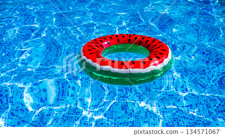 A bright ring-a float, with a watermelon, in the clear blue water of the pool, under the sunlight A bright ring-a float, with a watermelon, in the clear blue water of the pool, under the sunlight 134571067