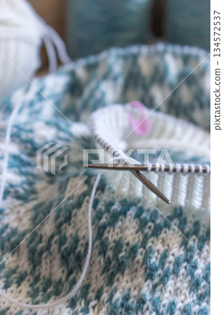 Norwegian knitted pattern. Knitting needles and beautiful knitting pattern. White and azure knitted pattern. Knitting hobby. Knitwear concept. Spot sweater process. Norwegian knitted pattern. Knitting needles and beautiful knitting pattern. White and azure knitted pattern. Knitting hobby. Knitwear concept. Spot sweater process. 134572537