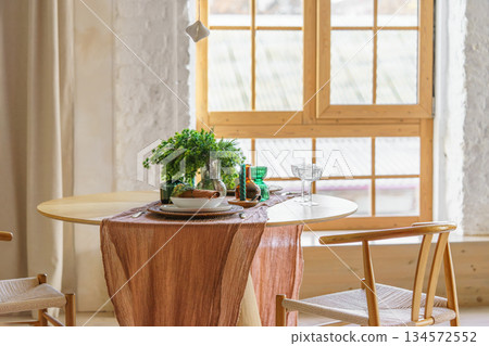 Cozy Scandinavian Christmas dining setting on table with natural decor on wide window background 134572552