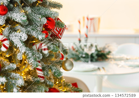 Frosted Christmas tree decorated with sparkling light and red ornaments on blurred dining background Frosted Christmas tree decorated with sparkling light and red ornaments on blurred dining background 134572589