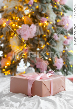 Soft pink Christmas gift box with ribbon on blurred holiday festive lights bokeh background Soft pink Christmas gift box with ribbon on blurred holiday festive lights bokeh background 134572592