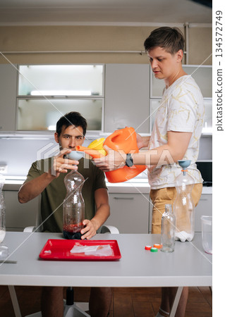 Two biology students preparing fertilizer solution with watering can, funnel and plastic bottles in lab, showcasing approach to botanical research. Concept of healthy sustainable cultivation. 134572749