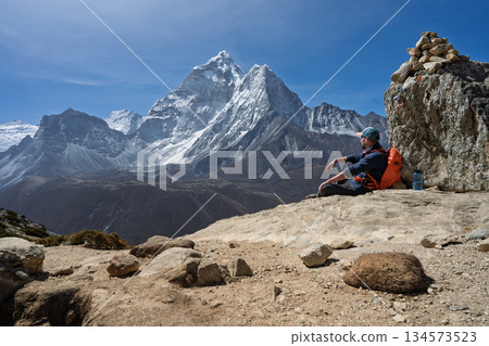 Hiker resting by cairn viewing Ama Dablam peak on Everest Trek, Nepal Hiker resting by cairn viewing Ama Dablam peak on Everest Trek, Nepal 134573523