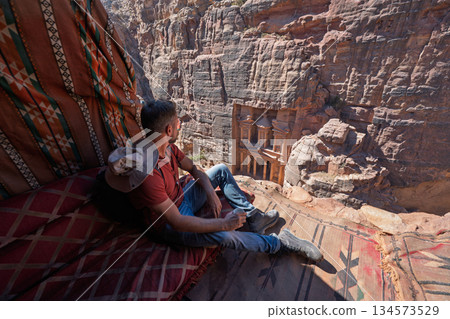 Tourist drinking tea in Bedouin tent overlooking Petra Treasury, Jordan Tourist drinking tea in Bedouin tent overlooking Petra Treasury, Jordan 134573529