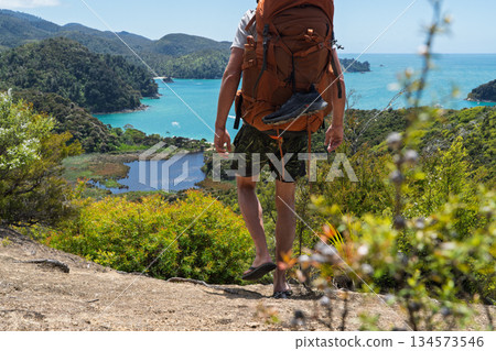 Hiker with backpack and flip flops walking Abel Tasman Coast Track, NZ 134573546