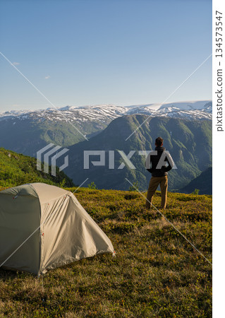 Hiker wild camping overlooking mountains at sunset, Odda, Norway 134573547