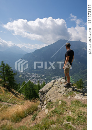 Hiker standing on cliff edge viewing Courmayeur town, Italian Alps Hiker standing on cliff edge viewing Courmayeur town, Italian Alps 134573555