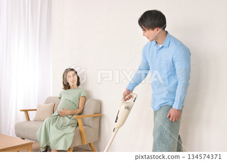 一位年輕男子一邊愉快地吸塵，一邊和孕婦聊天。 134574371
