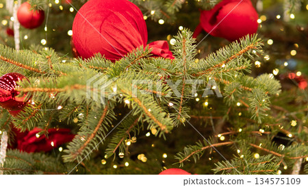 Close up red bauble on fir with glossy surface and subtle glitter bokeh highlights, boutique catalog styling, modern minimalist holiday mood, editorial closeup for luxury decor 134575109