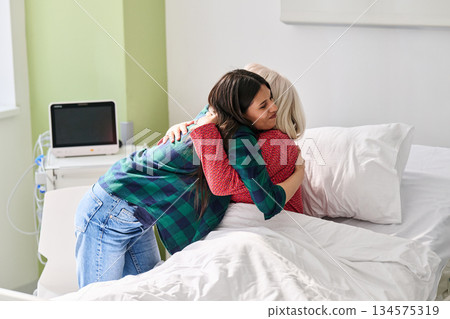 Woman hugs her mother in hospital bed showing love and support during recovery process Woman hugs her mother in hospital bed showing love and support during recovery process 134575319