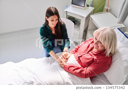 Caregiver provides support to elderly patient in hospital during daytime visit 134575342