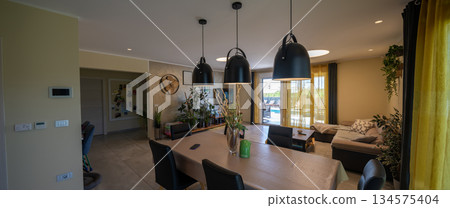 Bright modular house interior with modern open-plan living and dining room, large windows, indoor plants and cozy decor creating a warm, contemporary family home atmospher 134575404