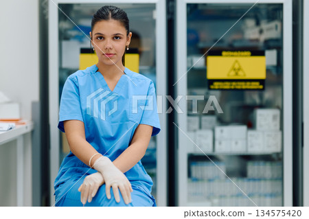 A medical professional is seated in a clinical environment, wearing blue doctor and gloves, ready to assist with patient care or medical tasks in a healthcare facility. 134575420