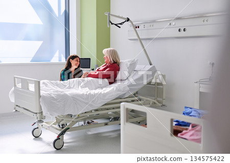 Woman visits patient in hospital room during daytime, sharing a moment of care and support in a bright and clean environment Woman visits patient in hospital room during daytime, sharing a moment of care and support in a bright and clean environment 134575422