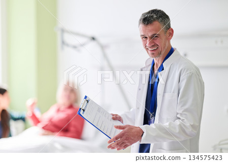 Smiling doctor interacts with patients in a bright hospital room during a morning shift Smiling doctor interacts with patients in a bright hospital room during a morning shift 134575423