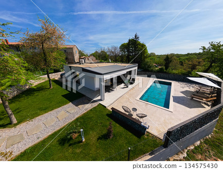 Aerial view of a modern modular house with flat roof, swimming pool, and patio. Contemporary prefabricated home architecture featuring sustainable design and outdoor living space 134575430
