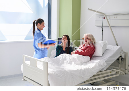 Nurse engages with patients in a modern hospital room during a morning visit 134575476