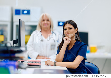 Medical professionals working together in a lab setting during daytime with computers and equipment nearby Medical professionals working together in a lab setting during daytime with computers and equipment nearby 134575479