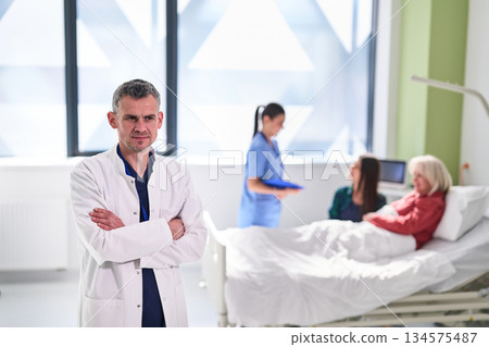 Doctor in a hospital room oversees nurses with patients during a routine check-up on a sunny morning 134575487