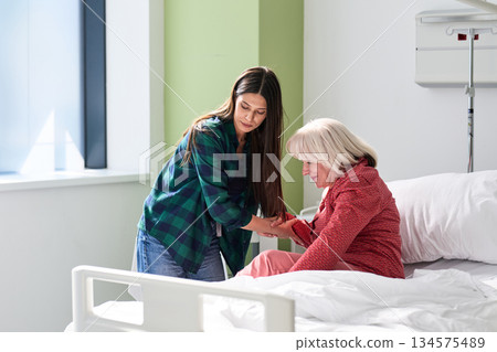 Caregiver assists elderly woman in hospital room during daytime visit for emotional support and companionship 134575489