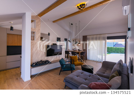 Modern open-plan living and dining area with an integrated kitchen, featuring a comfortable sofa, stylish armchairs, and a bar-height dining table. Wooden floors and ceiling beams enhance this Modern open-plan living and dining area with an integrated kitchen, featuring a comfortable sofa, stylish armchairs, and a bar-height dining table. Wooden floors and ceiling beams enhance this 134575521