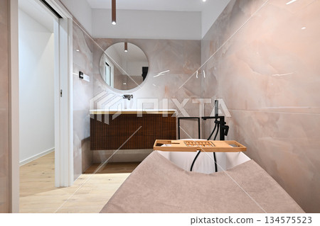 Luxurious modern bathroom featuring a sleek freestanding bathtub with a caddy, elegant vanity with sink and mirror, and a contemporary toilet. Soft tiled walls and wooden flooring create a spa-like 134575523