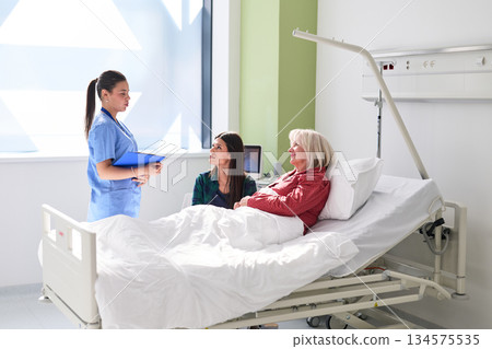 Nurse discusses care with family member at hospital bedside during day shift Nurse discusses care with family member at hospital bedside during day shift 134575535