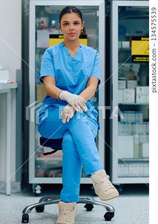 A medical professional is seated in a clinical environment, wearing blue doctor and gloves, ready to assist with patient care or medical tasks in a healthcare facility. 134575539
